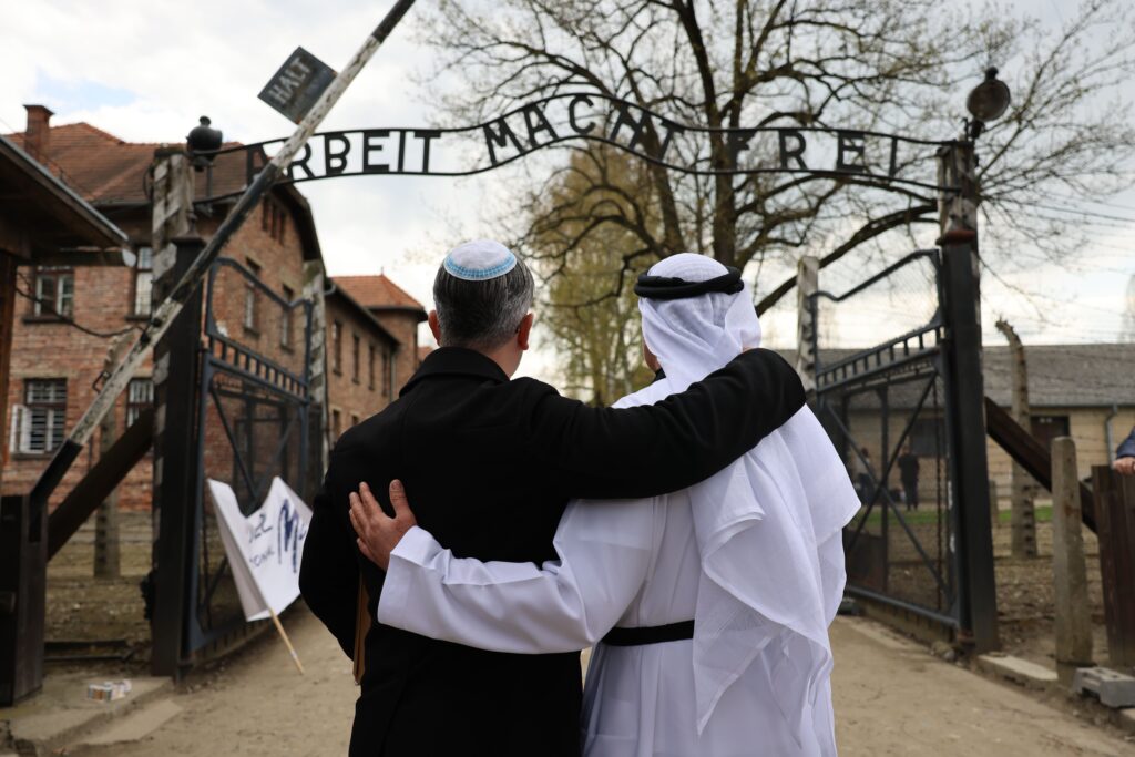 Eitan Neishlos standing with his arm around Ahmed Obaid AlMansoori at the entrance of Auschwitz