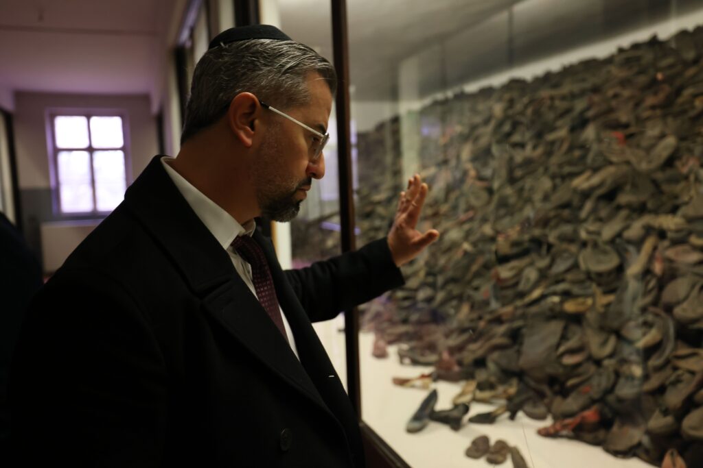 Eitan Neishlos touching glass in front of children's shoes at Auschwitz